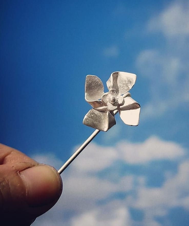 Silver flower pin being held up to the sky