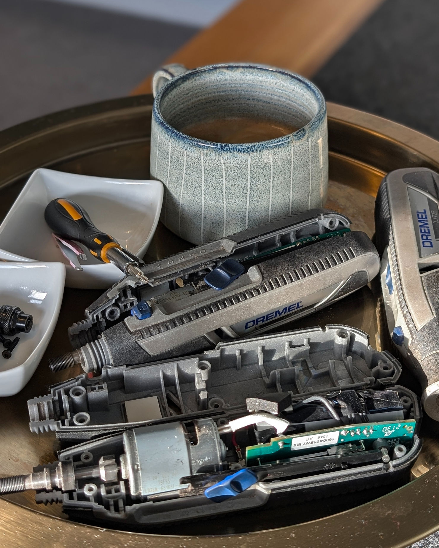 Three Dremel rotary tools taken apart on a tray with a mug of coffee