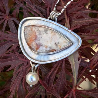 Front of burn agate stone and silver necklace over seaweed